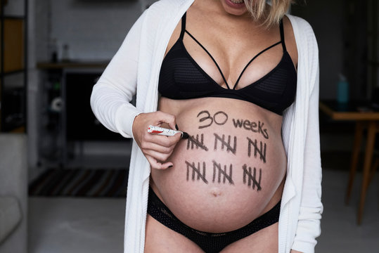Close-up of pregnant woman painting tally marks on her belly