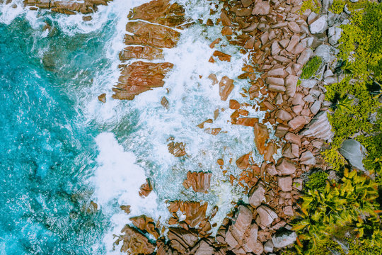 Aerial drone photo of Seychelles tropical beach Anse Cocos at La Digue Island. White rolling waves splash granite coastal rocks. Travel and vacation concept