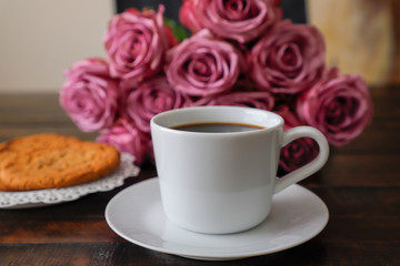 cup of coffee and roses on wooden table. Holiday concept, a bouquet of roses for a birthday, a bouquet of flowers on his girlfriend in the morning.