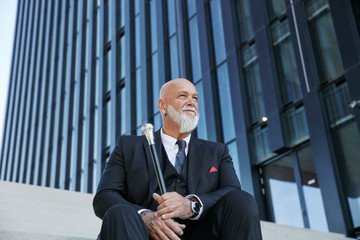 Elegant businessman with walking cane, sitting on stairs in the city
