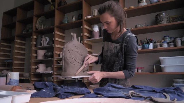 a beautiful woman ceramist removes excess clay from her product dolly shot