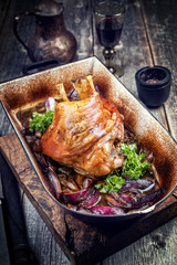 Traditional Bavarian schweinshaxe with onion as closeup in a rustic stewpot on an old wooden board