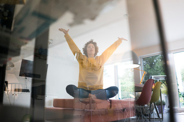 Woman sitting on couch at home in yoga pose
