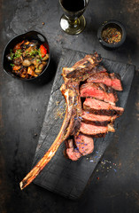 Traditional barbecue dry aged wagyu tomahawk steak sliced with ratatouille as top view on a rustic carbonized wooden board