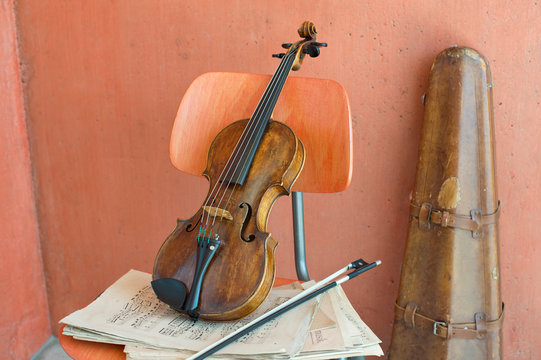 Violin, bow and sheet music on wooden chair with violin case in the background