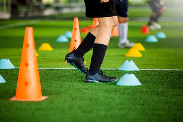 selective focus to kid soccer team jogging between yellow and blue marker cones for football training on green artificial turf