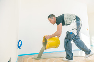 Plasterer during floor covering works with self-levelling cement mortar