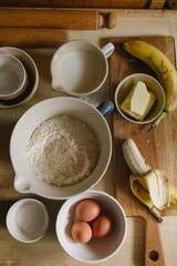 Ingredients to prepare a bunch of banana muffins are displayed over a wooden board,too view, natural light