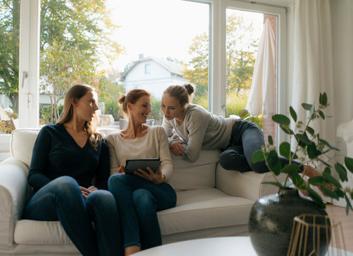 Happy mother with two teenage girls using tablet on couch at home