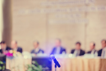 Blurry of microphone with chairman of the meeting and executive committee background in auditorium for shareholders meeting or seminar event, Annual shareholder meeting
