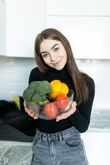 Smiling young woman holding vegetables standing in kitchen