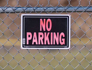 Faded old No Parking sign on wire fence
