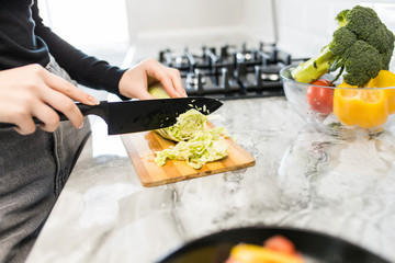 Woman hands cutting vegetables for salad in the kitchen. Close up.