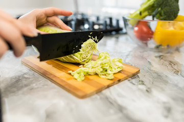 Woman hands cutting vegetables for salad in the kitchen. Close up.