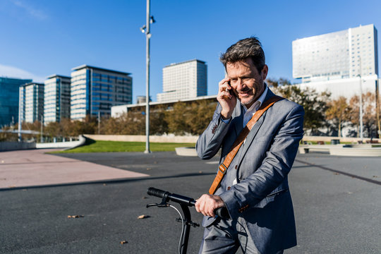 Mature businessman commuting in the city with his kick scooter, using smartphone