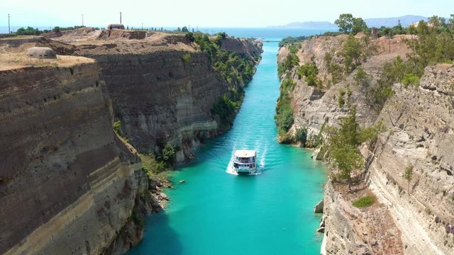 Beautiful scenery of the Corinth Canal in a bright sunny day against a blue sky. Among the rocks floating white ship in turquoise water. Greece