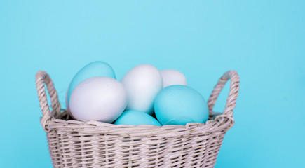 Traditional painted Easter eggs in white basket, pastel color background. Spring and Easter holiday concept.