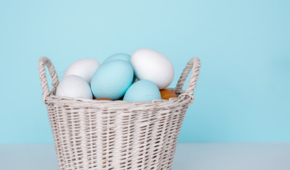 Traditional painted Easter eggs in white basket, pastel color background. Spring and Easter holiday concept.