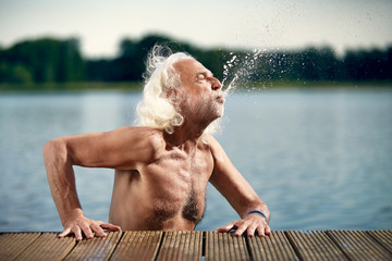 Senior man with white hair leaning on jetty splashing with water
