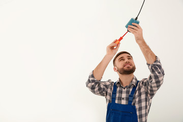 Electrician with screwdriver repairing ceiling lamp against white background
