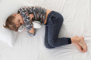 Cute boy with toy sleeping on bed, above view