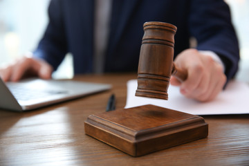 Judge with gavel at table in courtroom, closeup. Law and justice concept