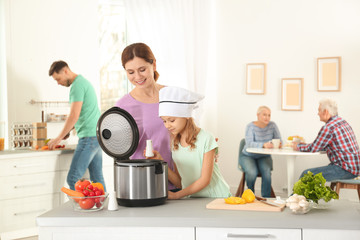 Mother and daughter preparing food with modern multi cooker in kitchen