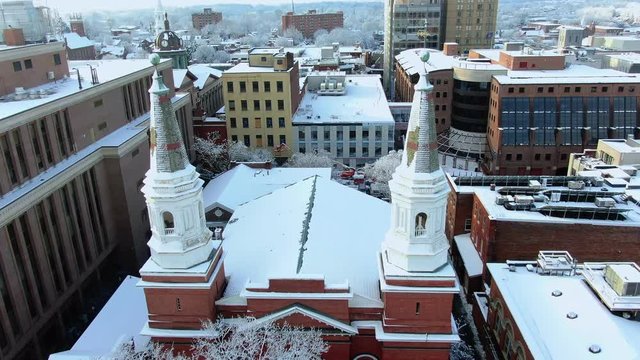 Flying between church steeples in winter above snow covered Lancaster, Pennsylvania, First Reformed Church United Church of Christ, downtown in background with the Sheriff's office and Courthouse