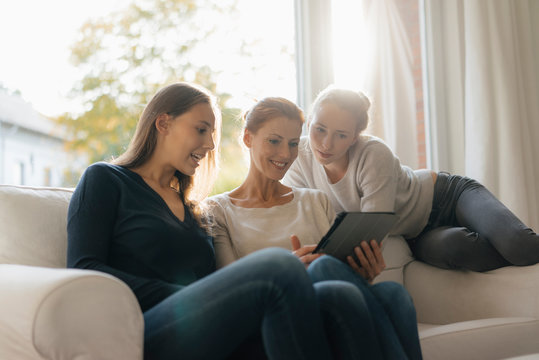 Happy mother with two teenage girls using tablet on couch at home