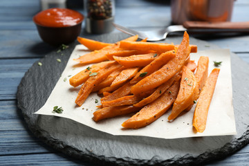 Slate plate with tasty sweet potato fries on wooden table