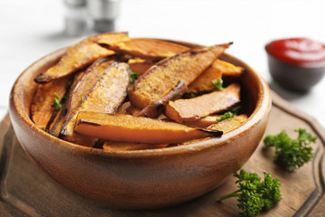 Bowl with tasty sweet potato fries on wooden board, closeup