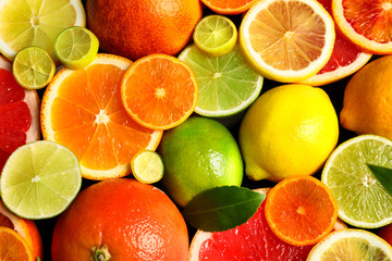 Sliced and whole citrus fruits with leaves as background, top view
