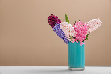 Beautiful hyacinths in blue vase on table against color background, space for text. Spring flowers