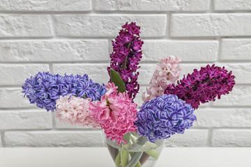 Beautiful hyacinths in glass vase on table against brick wall. Spring flowers