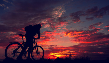Obraz premium cyclist with a bicycle, in the background fiery sunset.