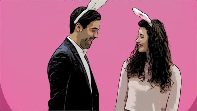 Young sexy couple on pink background. With hackneyed ears on the head. During this man gives a soft toy hare and colored decorative eggs to his wife. Having kissed looking at the camera. Easter