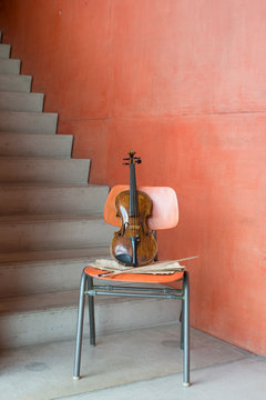 Violin, bow and sheet music on wooden chair at staircase