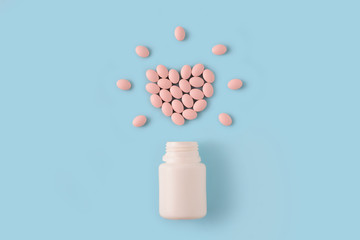 Pink pills in shape of heart and bottle on blue background. Medical pharmacy concept.