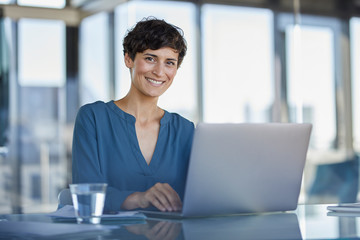 Portrait of confident businesswoman sitting at desk in office with laptop