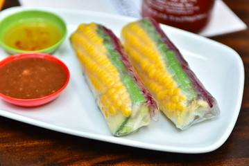 Traditional Vietnamese cuisine dish - fresh vegetable spring rolls wrapped in transparent rice paper with corn, beetroot, avocado, vermicelli, mint and carrots inside served with spicy sauces