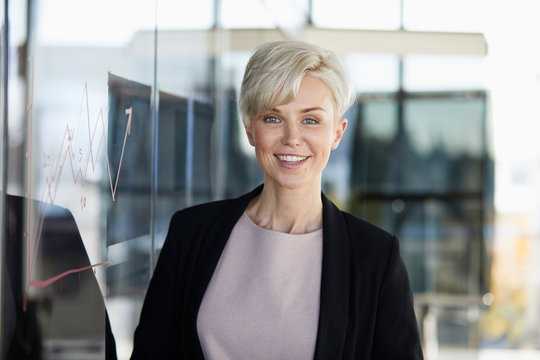 Portrait of smiling businesswoman next to chart on glass pane in office