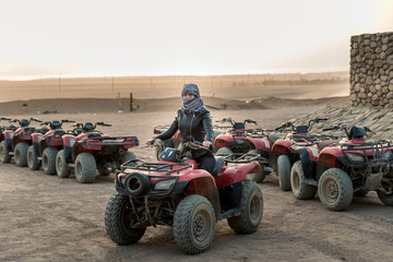 girl with a closed handkerchief of faces sitting on a quad bike against the background of the sun...