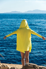 Travel and leisure, a girl in a yellow jacket stands against the blue sea with her arms spread to the sides