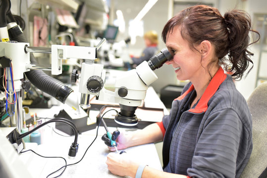 Woman using a microscope for the quality control in the manufacturing of circuit boards for the electronics industry