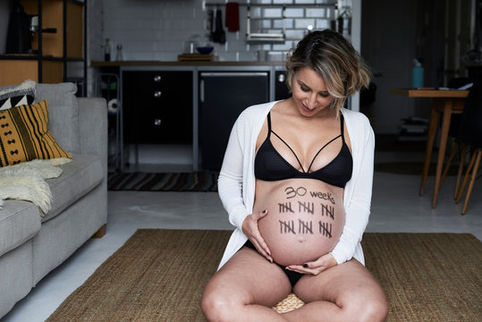 Pregnant woman sitting on the floor at home looking at tally marks on her belly
