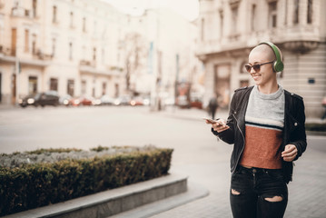 Young modern woman with bald hairstyle listening to her favorite music over her big green...