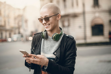 Young modern bald woman talking on her cell phone, enjoying a beautiful day outside in an urban...