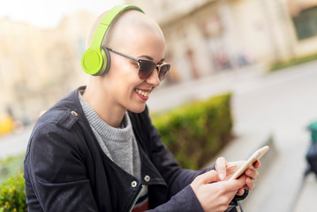 Young modern woman with bald hairstyle listening to her favorite music over her big green...