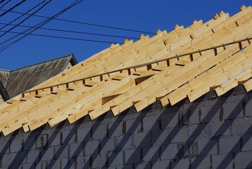 construction of a private house of brown wooden boards and gray bricks against a blue sky