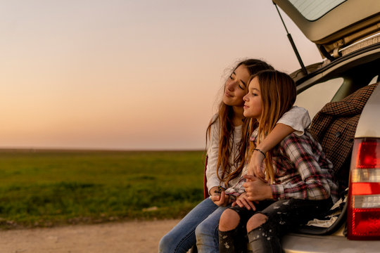 Two happy sisters sitting at opened tail watching sunset together